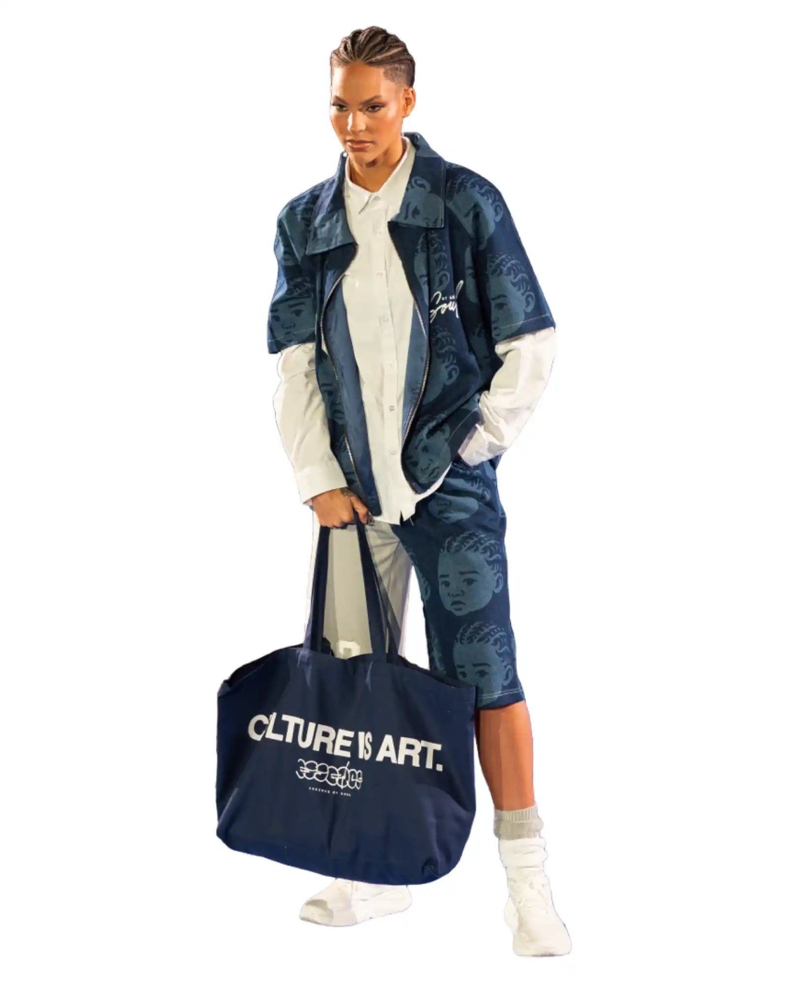 A model wearing a denim jacket and shorts with a white long-sleeved shirt, holding a navy blue tote bag.